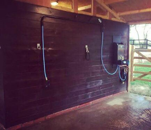 Wall-mounted shower system in a barn setting with wooden walls and a roof.