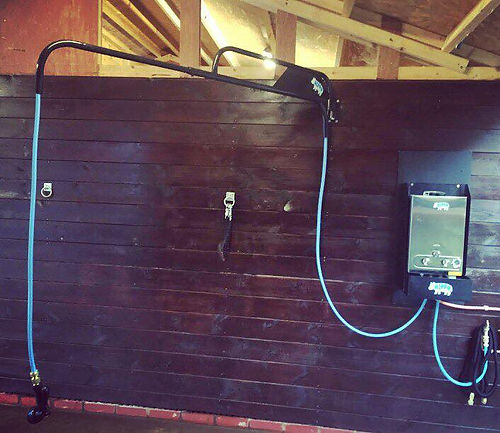 Outdoor shower system with hose and control panel mounted on a wooden wall.