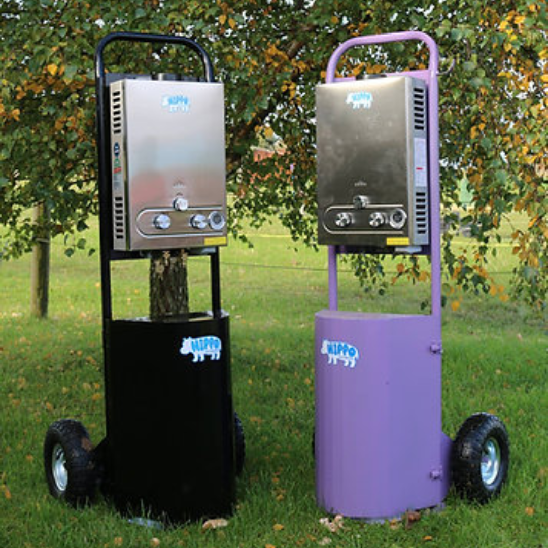 Two portable gas hippo showers, one black and one purple, on wheels with a grassy background.