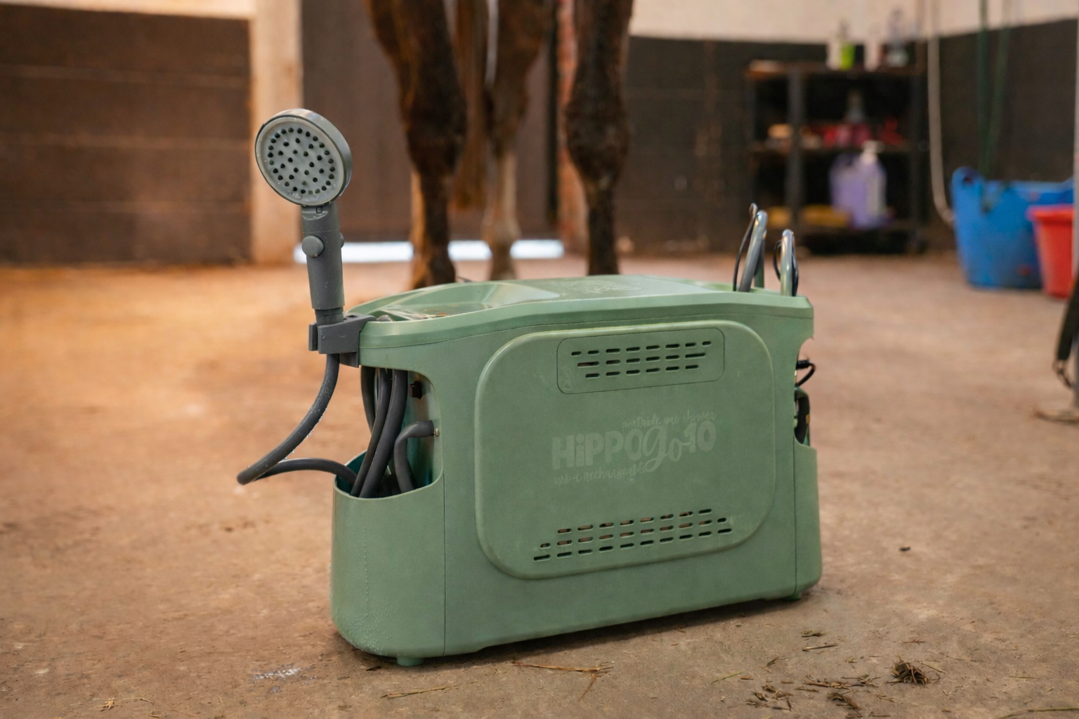 Green grooming machine with a hose attachment on a concrete floor, with a horse in the background.