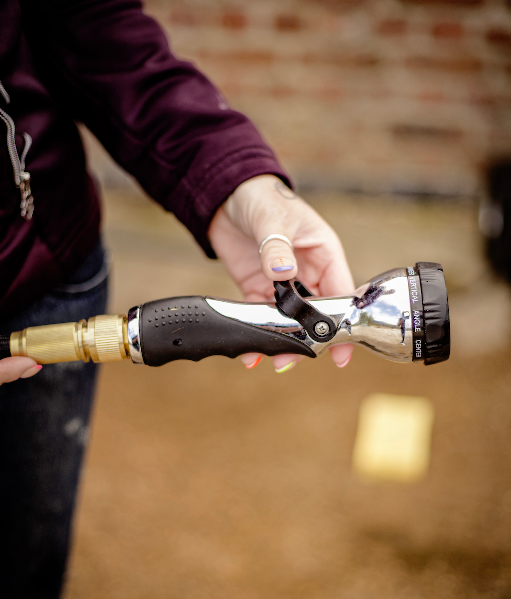 Person holding a shower head with a black handle against a blurred background