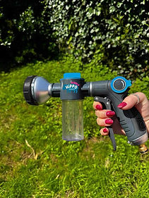 Hand holding a Wippit garden hose nozzle against a grassy background